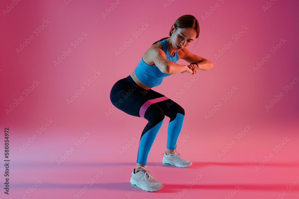 Woman performs fitness exercises with resistance band on studio background. High quality photo