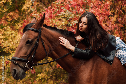 A young sexy woman lies on top of a horse. Horseback riding in the autumn forest