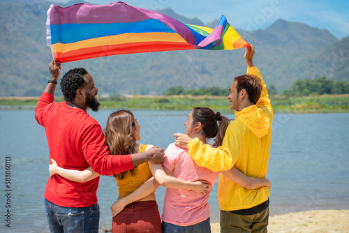 Back view. Young diversity people having fun holding LGBT rainbow flag on the beach. Supporters of the LGBT community