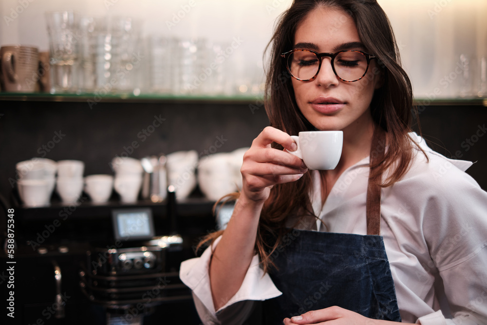 Portrait of a waitress standing at coffee shop and trying out coffee.