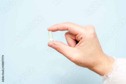 Doctor's hand holding a fish oil capsule (Omega 3) or pill isolated on light blue background