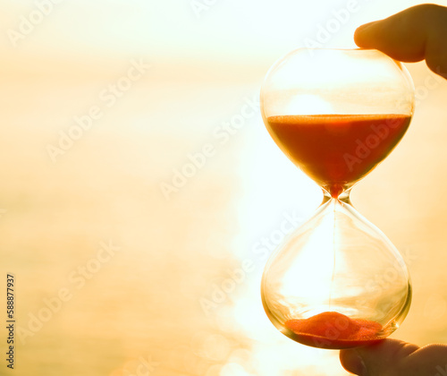 male hand holding Hourglass at sunset sea background with empty copy space. sun set sky. time is money.