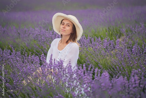 A young relaxed girl breathes fresh air while sitting in a hat in a lavender field on a sunny day.
