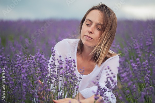 A young relaxed girl breathes fresh air while sitting in a hat in a lavender field on a sunny day.