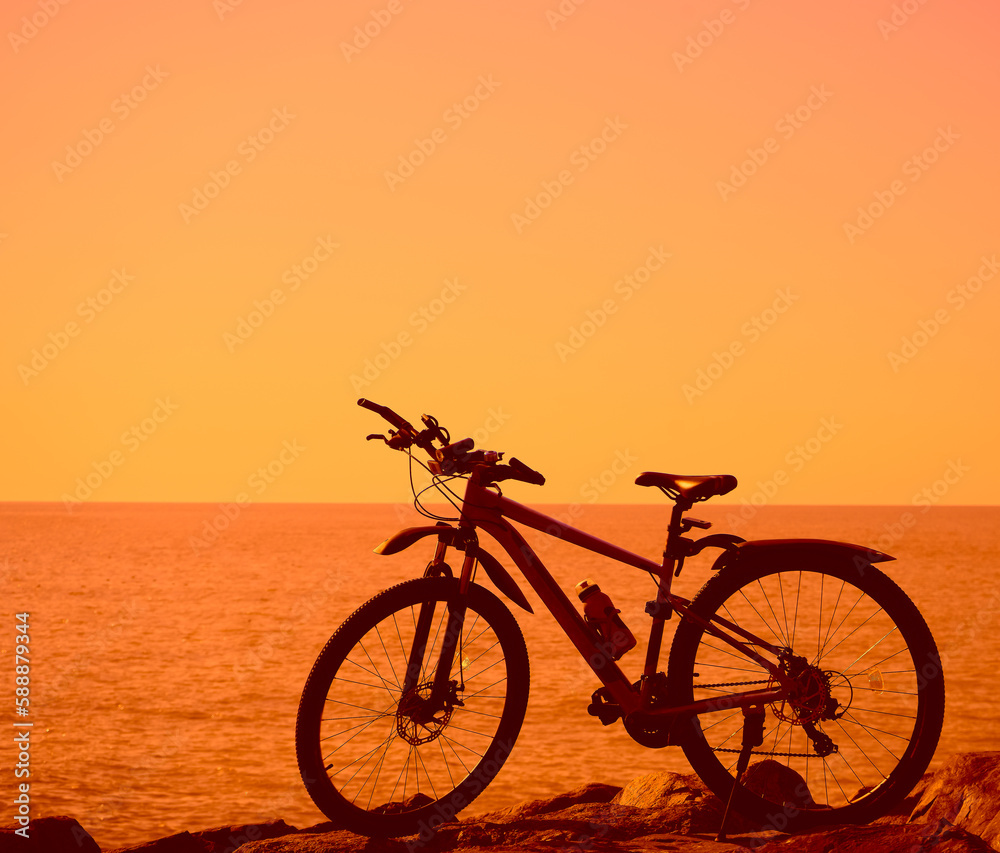 silhouette of one, alone blue modern bike stands in big stones. Black Sea coast. Batumi, Georgia. Mountain bike parked on the beach. no people. yellow , orange sunset sky. silhouette of one, alone blue modern bike stands in big stones. Black Sea coast. Batumi, Georgia. Mountain bike parked on the beach. no people. yellow , orange sunset sky.