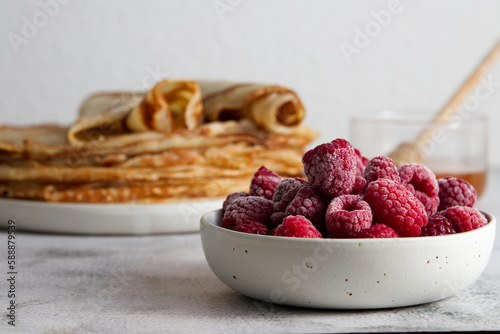 Stack of fresh crepes with honey and raspberries on the table copy space photo