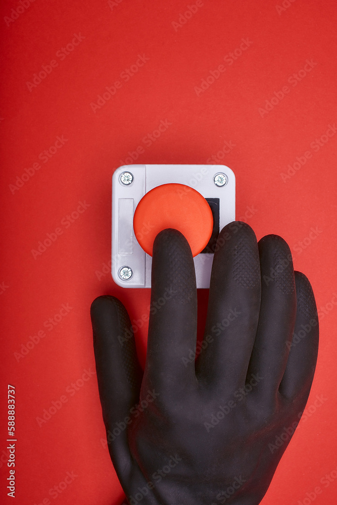 The hand in black resin glove, which pushes the emergency button at the red background at the top view The hand in black resin glove, which pushes the emergency button at the red background at the top view