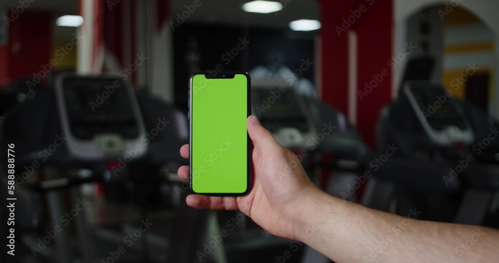 back view of fitness woman using green screen smart phone at home. Woman preparing for workout using smart phone.Woman using mobile phone while resting during fitness training.