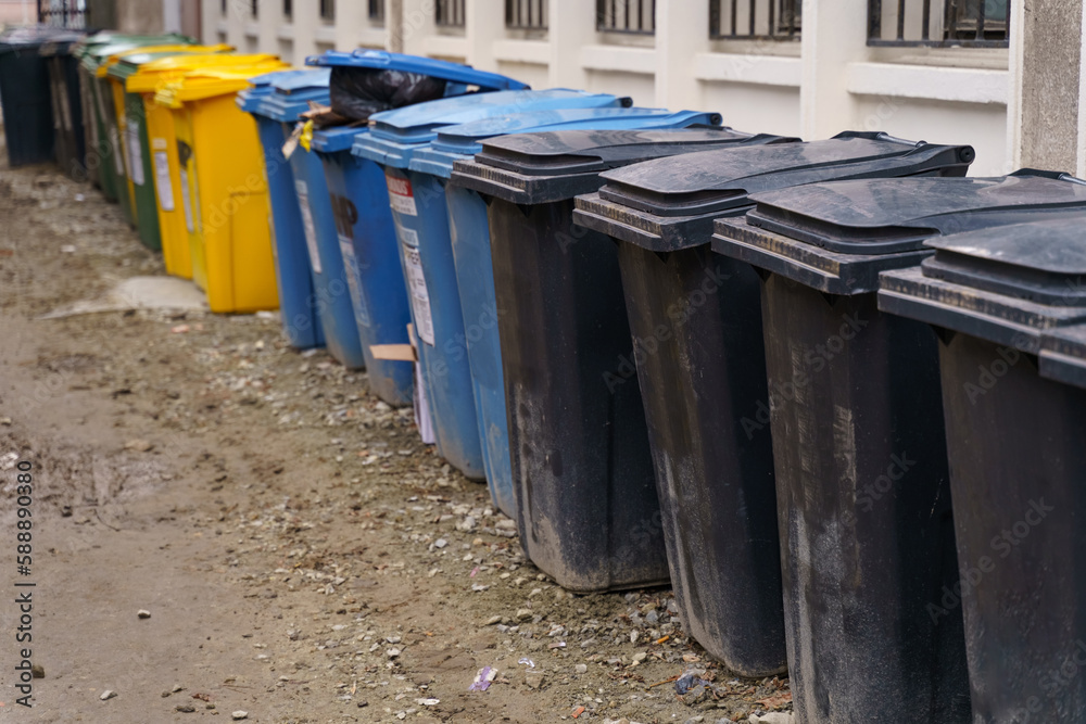 Rows of garbage cans of different colors in an alley in the city center, near a construction site Rows of garbage cans of different colors in an alley in the city center, near a construction site