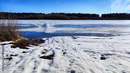 Spring landscape with water, ice, snow on river, trees without leaves and blue sky in the background in sunny day. Ice drift and flood on the river with sun © keleny