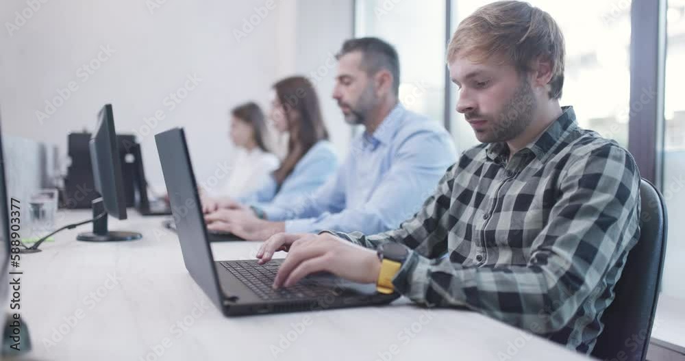 People sitting in a row in office working on laptop and desktop computers. Bussiness colleagues team. Shallow depth of field video recorded at 50fps. People sitting in a row in office working on laptop and desktop computers. Bussiness colleagues team. Shallow depth of field video recorded at 50fps.