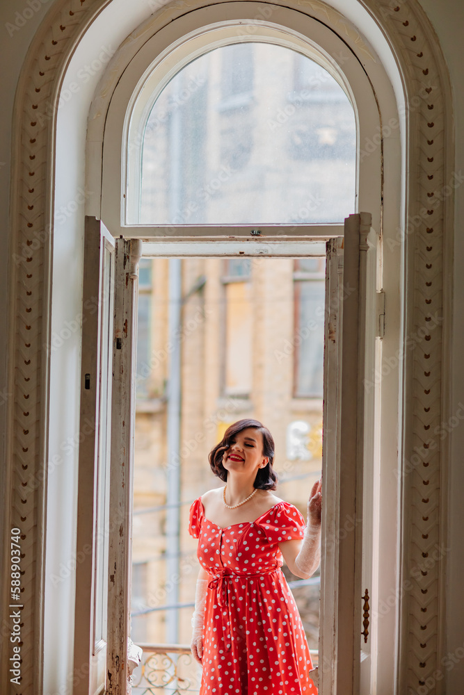 Fototapeta premium a beautiful and happy brunette women in red retro dress in the balcony doorway 