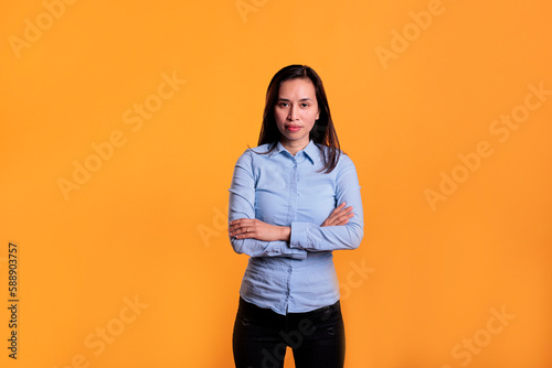 Positive smiling woman standing with arm crossed in studio over yellow background, being confident and carefree on camera. Cheerful filipino model with joyful expression having fun, enjoying free time © DC Studio