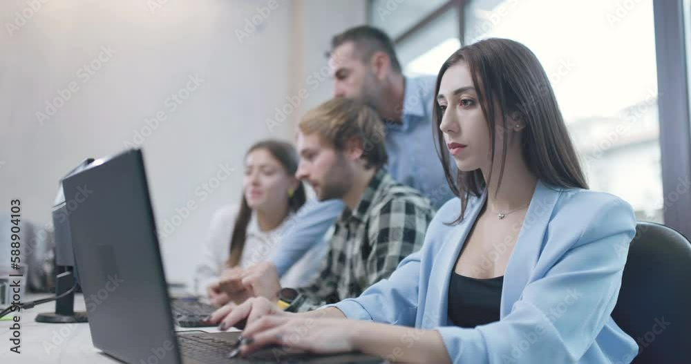 Woman in an office working on laptop computer. Bussiness colleagues team working together in the background. Shallow depth of field. Woman in an office working on laptop computer. Bussiness colleagues team working together in the background. Shallow depth of field.