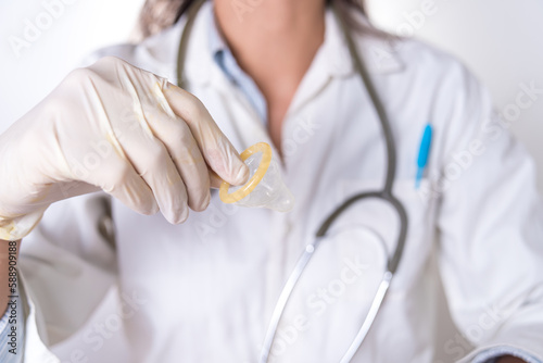 A woman wearing a white coat and gloves holds a condom in her hand to prevent the spread of AIDS.