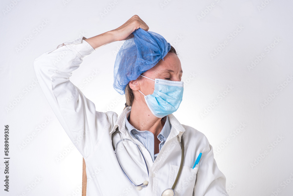 Una mujer con mascarilla y estetoscopio se quita la cofia de la cabeza, cansada, doctora Una mujer con mascarilla y estetoscopio se quita la cofia de la cabeza, cansada, doctora