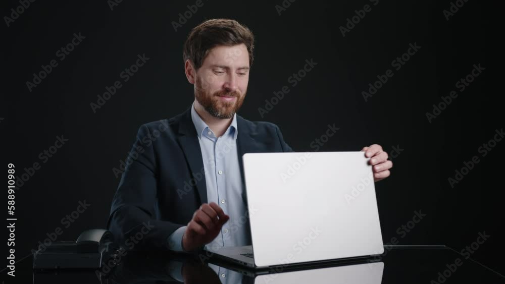A man in a black suit working on his laptop and then closing it with a smile. He looks happy and pleased. He is in a black room. High quality 4k footage A man in a black suit working on his laptop and then closing it with a smile. He looks happy and pleased. He is in a black room. High quality 4k footage