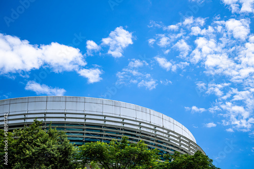 Round building with beautiful green vegetation in the foreground and blue sky with few clouds.