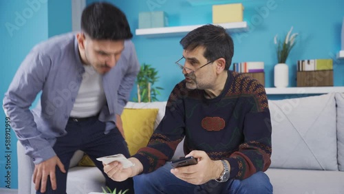 Son helping father who can't use phone.
The father cannot use the phone and the son describes it to him. They pay the bills together and the father thanks him.
