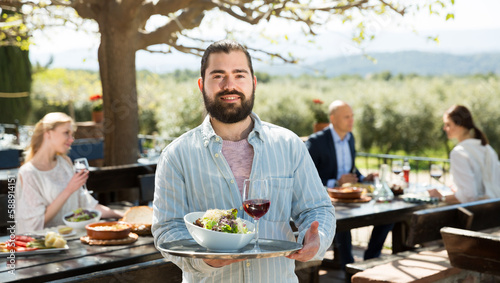 Adult beard waiter who is standing with order at country outdoor restaurant. High quality photo