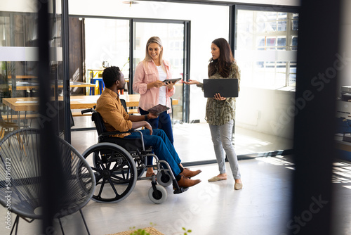 Diverse casual disabled businessman in wheelchair discussing work with colleagues in office photo