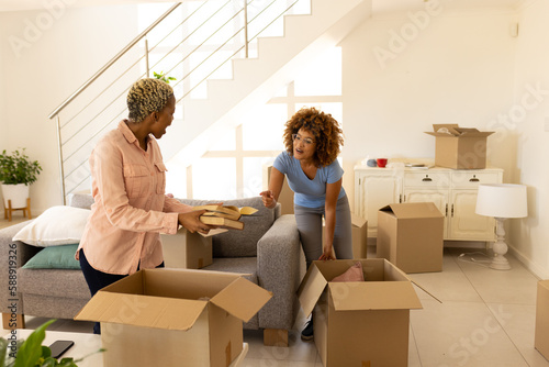 Multiracial lesbian couple surprisingly looking at books while unpacking boxes in new home photo