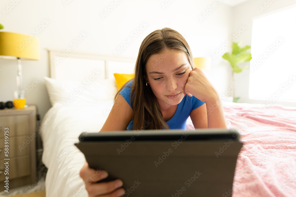 Happy caucasian teenager girl lying on bed and using tablet Happy caucasian teenager girl lying on bed and using tablet