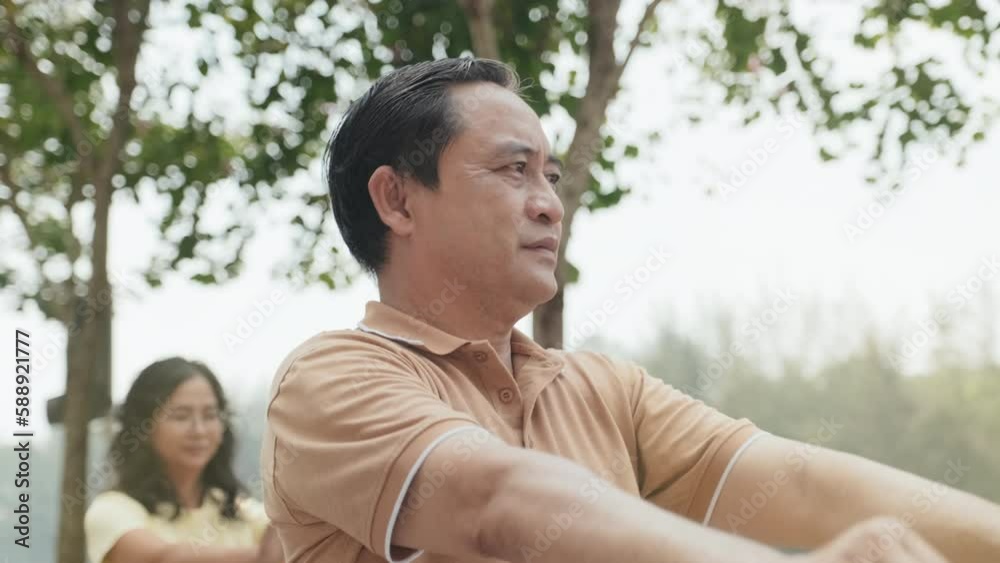 Tilt up shot of mature Asian man practicing Tai chi with group of people outdoors in park on summer day Tilt up shot of mature Asian man practicing Tai chi with group of people outdoors in park on summer day