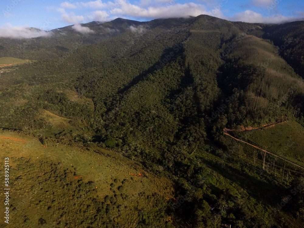 Aerial view of beautiful forest full of nature and pasture fields in Tremembé in Vale da Paraíba in São Paulo. Mountains and hills in sunny day. Lots of green and tropical vegetation. Drone. Sunset