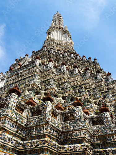 The main spire at the Wat Arun Temple, the Temple of Dawn, with its intricite facade of color is stretching towards a blue sky in Bangkok, Thailand.