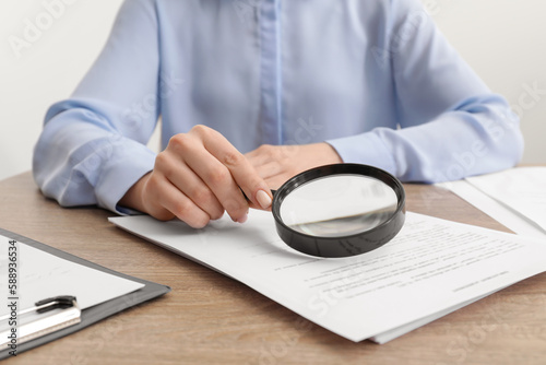 Woman looking at document through magnifier at wooden table, closeup. Searching concept