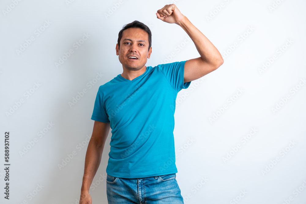 Fototapeta premium Hombre latino de playera azul festejando levantando el brazo con fondo blanco