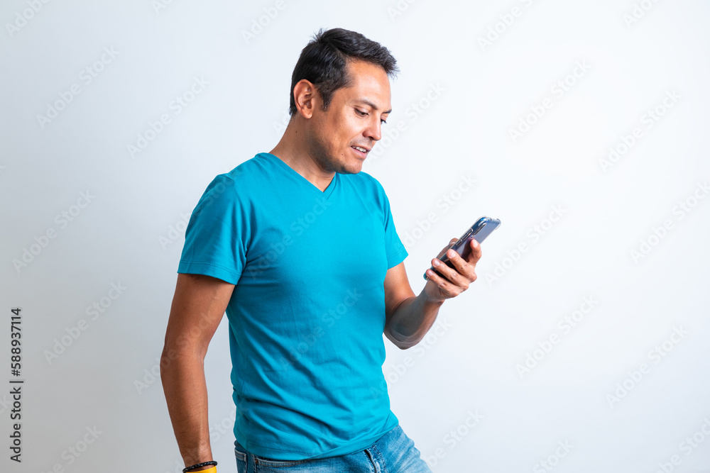 Hombre contento de piel morena de playera azul revisando el celular con fondo blanco Hombre contento de piel morena de playera azul revisando el celular con fondo blanco