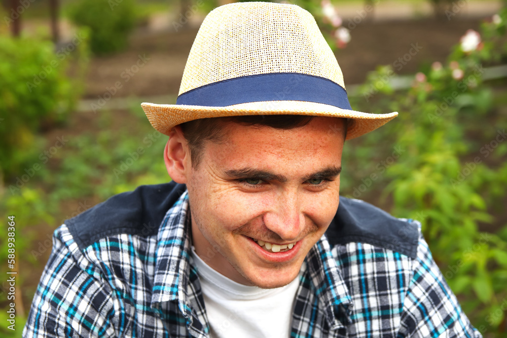 Smiling farmer in hat. Defocus farmer in hat working on field with greenhouse outdoor. Portrait of young Caucasian handsome happy man farmer in field and smiling. Out of focus