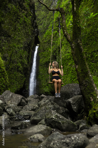 Girl hiker swings in front of a waterfall in Hawaii green jungle forest. 