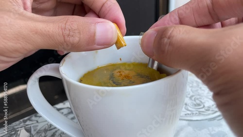 Male hand holding capsule and pouring turmeric powder into a cup. Use spoon to stir the cup.