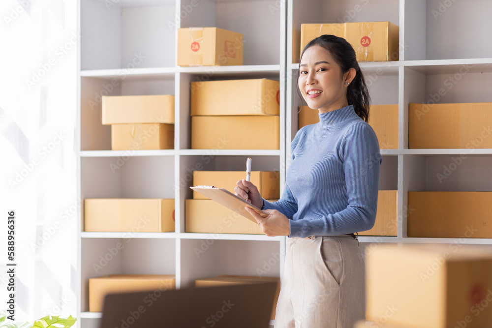 Asian Female entrepreneur starting a small business for SME online sales working with parcel boxes at home checking orders from the internet preparing for SME delivery. Asian Female entrepreneur starting a small business for SME online sales working with parcel boxes at home checking orders from the internet preparing for SME delivery.