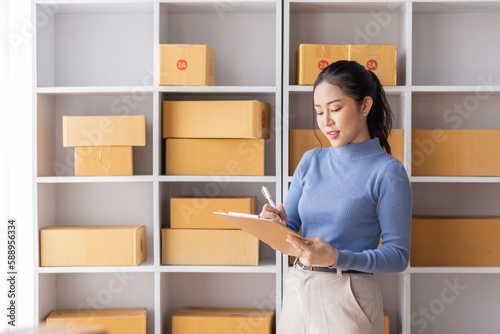 Asian Female entrepreneur starting a small business for SME online sales working with parcel boxes at home checking orders from the internet preparing for SME delivery.