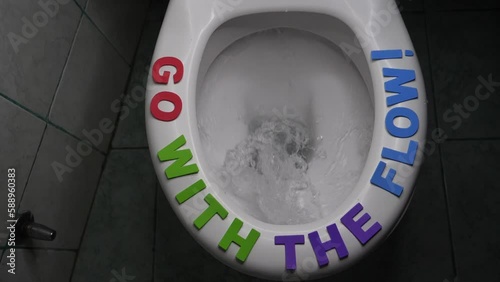 Go with the flow! text phrase on rim of toilet seat. Flow of water rushes into drain funnel. Inspiration Concept. Creative decoration. Motivation inspirational Inscription quote on toilet. Slow motion