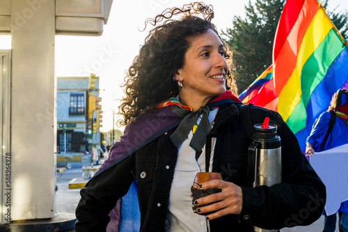 Woman drinking mate and holding a rainbow flag in an lgbtq pride march.