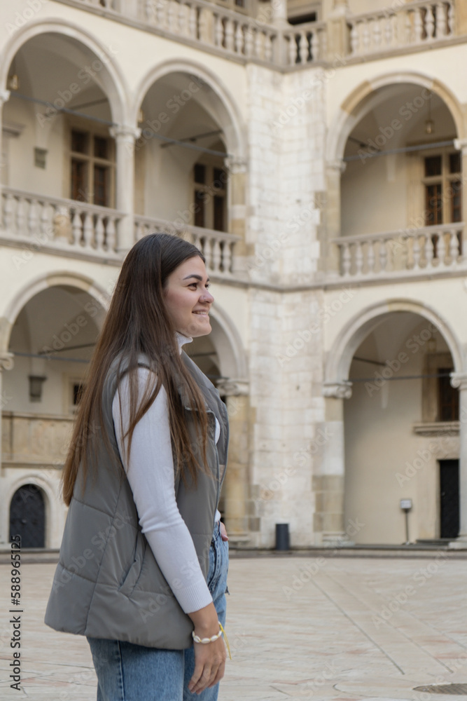 Fototapeta premium Female traveler in historical places looks around courtyard of landmark in Krakow Wawel castle. Tourist in historic place on sunny day. woman Tourism and blogging sharing live online for audience