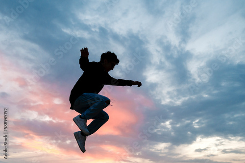 Silhouette of a person jumping outdoors with the sunset sky on background.