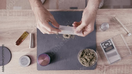 Top down view table, caucasian man rolls a marijuana joint in dealer environment