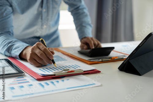 Businessman hand pressing calculator and preparing data while holding pen Analyze the chart Chart of investment in real estate projects and an auditor to calculate expenses with a tablet. © Phimwilai