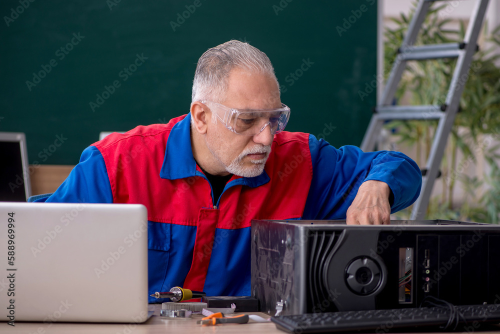 Old repairman repairing computers in the classroom Old repairman repairing computers in the classroom