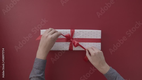 A young man's hands unwrap a gift package against a red background, capturing the Christmas and festive season.