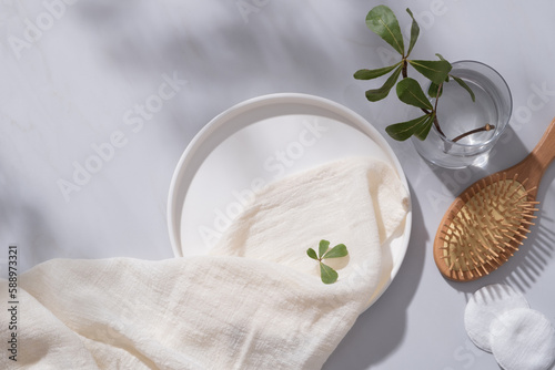 A round dish decorated with a white towel, cotton pads, wooden brush and a glass vase with tree branch. Empty space for natural beauty product advertising