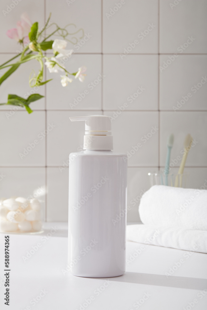 Front view of white bottle unlabeled in bathroom background with towel, toothbrush and flower branch on white tile wall. Mockup for cosmetic product with beauty concept. Front view of white bottle unlabeled in bathroom background with towel, toothbrush and flower branch on white tile wall. Mockup for cosmetic product with beauty concept.