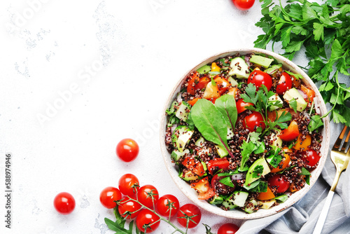 Quinoa tabbouleh salad with red cherry tomatoes, orange paprika, avocado, cucumbers and parsley. Traditional Middle Eastern and Arabic dish. White table background, top view photo