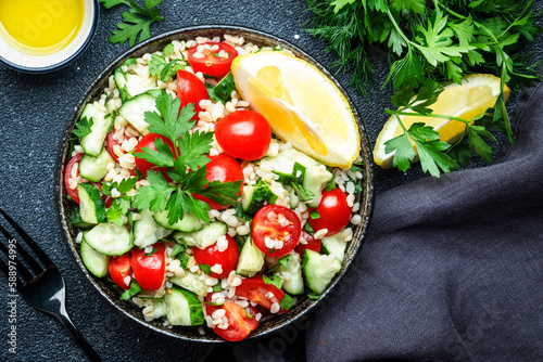Bulgur tabbouleh salad with red cherry tomatoes, cucumbers, parsley and lemon dressing. Traditional Middle Eastern and Arabic dish. Bllack kitchen table background, top view